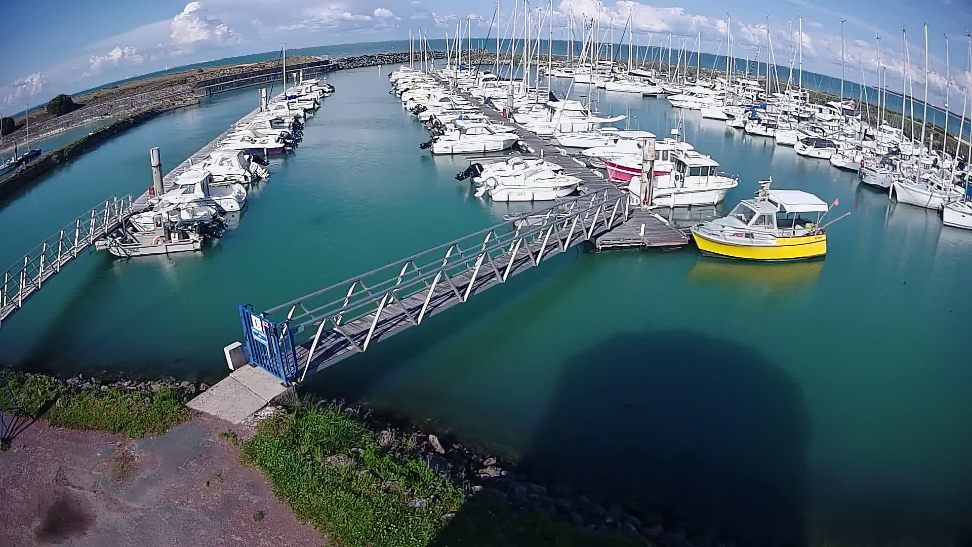 A marina with numerous boats docked along multiple piers under a partly cloudy sky.