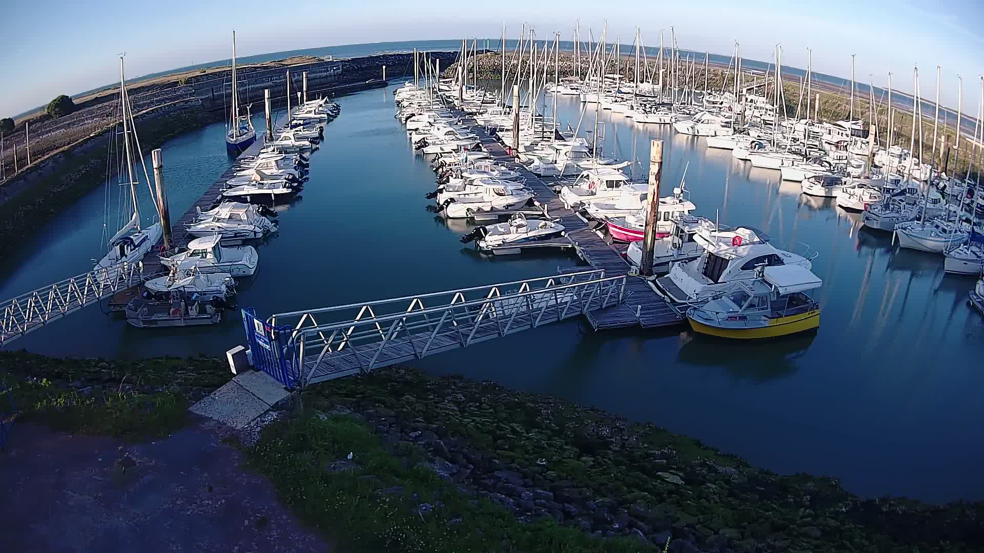 A marina filled with numerous sailboats and motorboats on a calm, sunny day.