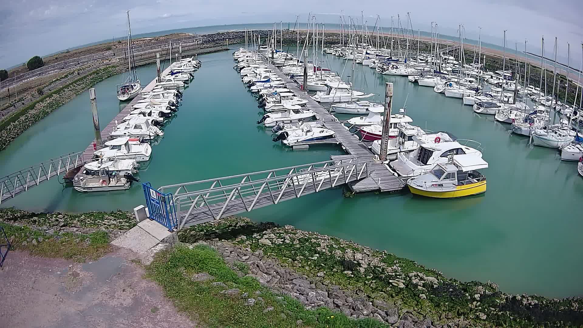 A marina filled with numerous boats of varying sizes, docked along several piers, under a partly cloudy sky.