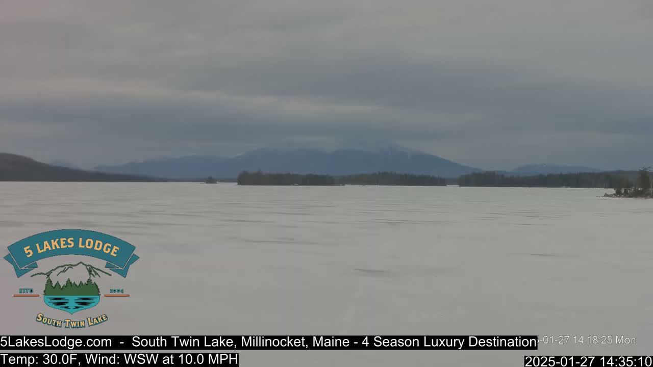 A snow-covered lake stretches to distant mountains under an overcast sky.