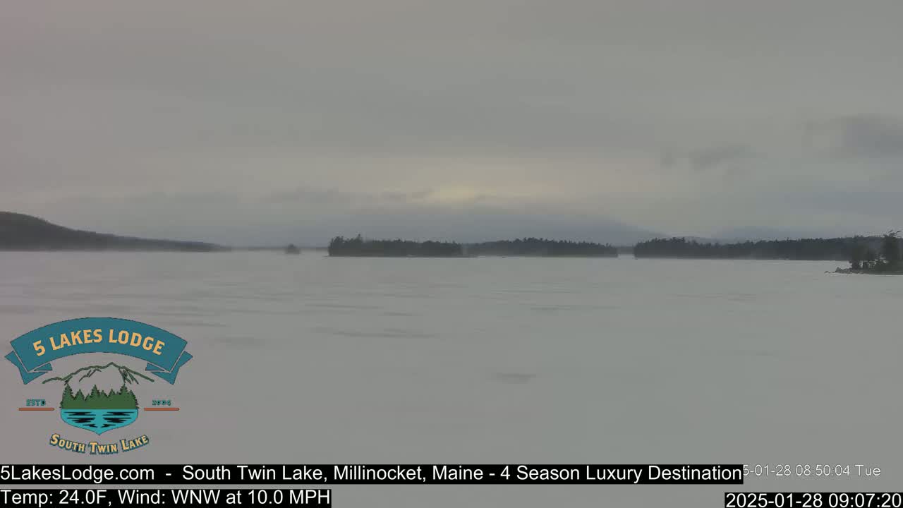 A hazy, overcast day shows a frozen lake with a distant treeline under a pale sky.