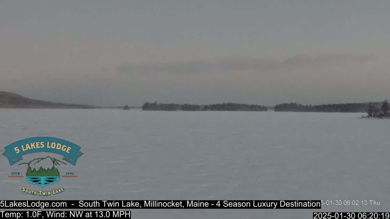 A snow-covered lake with a distant treeline under an overcast sky.