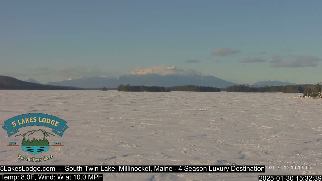 A snow-covered lake stretches to a distant mountain range under a clear, light blue sky.