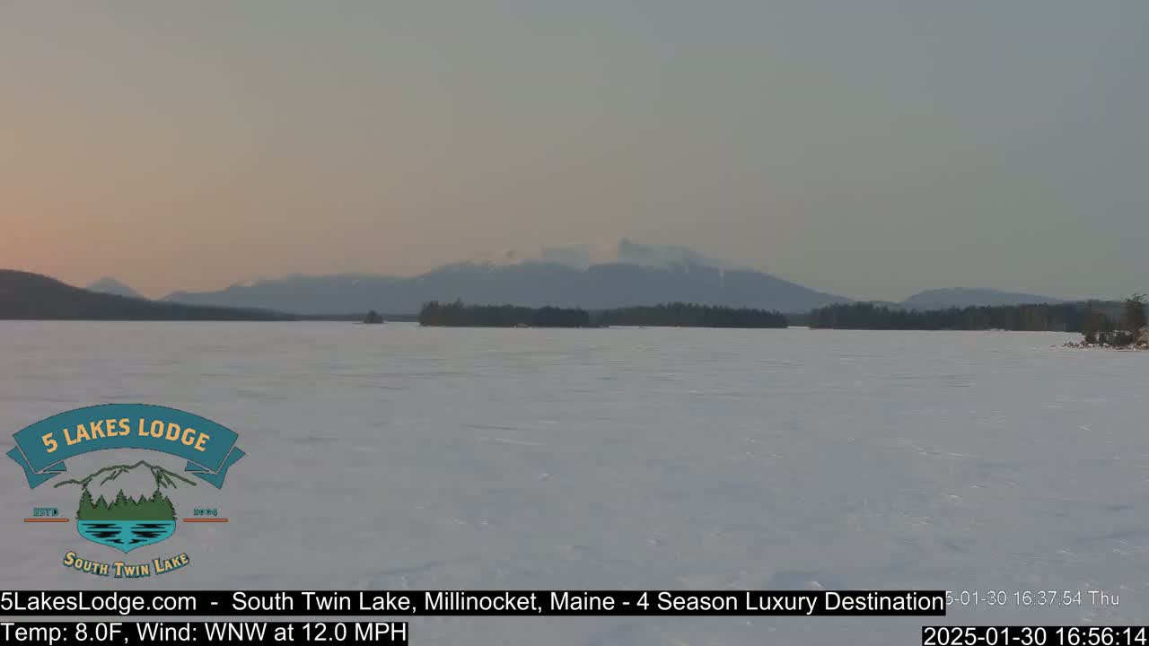 A frozen lake stretches towards distant mountains under a pale, dusky sky.