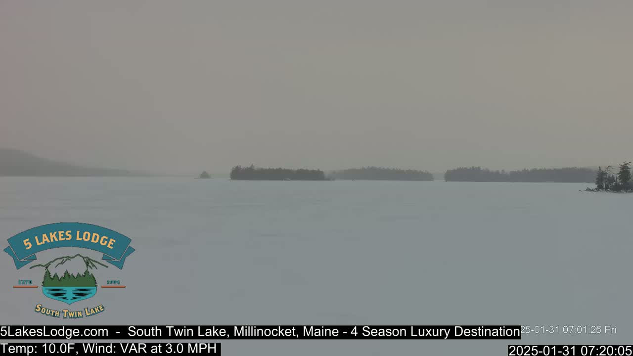 A snow-covered lake with hazy conditions and distant tree lines is visible under a gray sky.