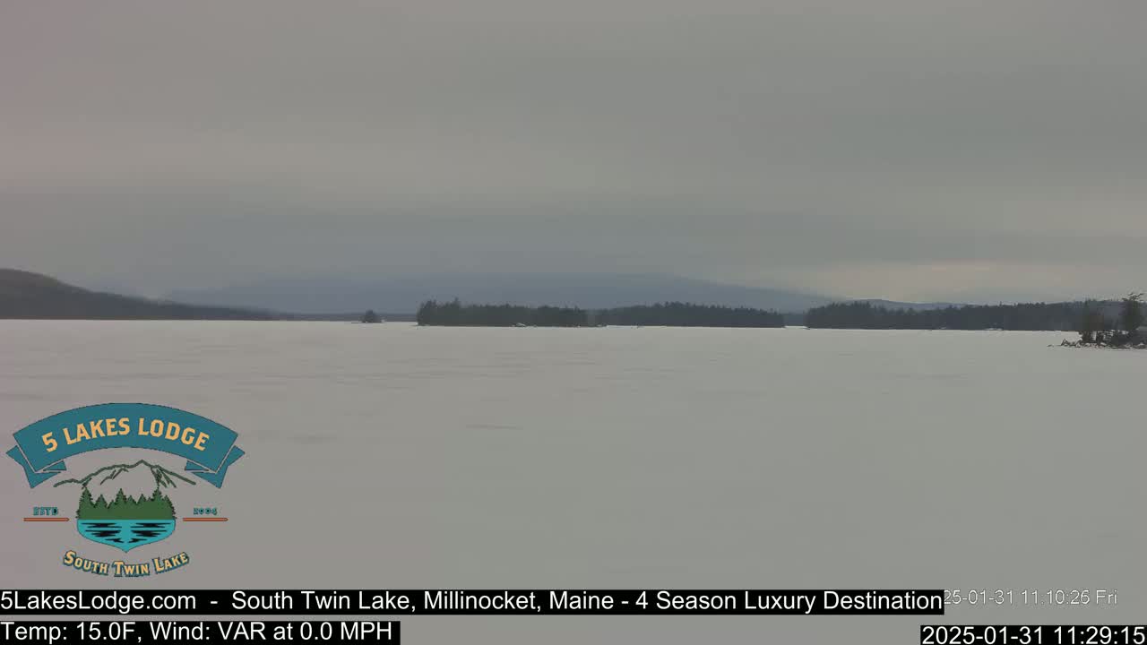A frozen lake stretches to a distant, snow-covered treeline under an overcast sky.