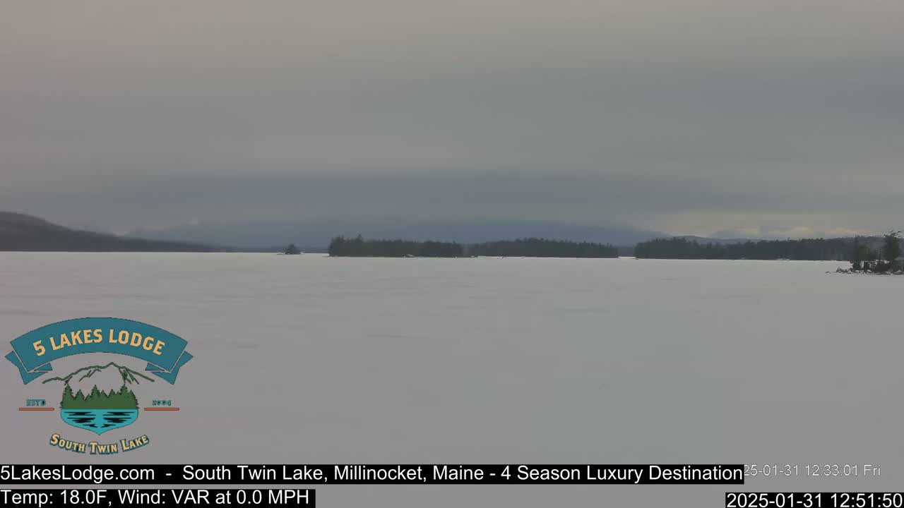 A snow-covered lake stretches to a dark treeline under an overcast sky.