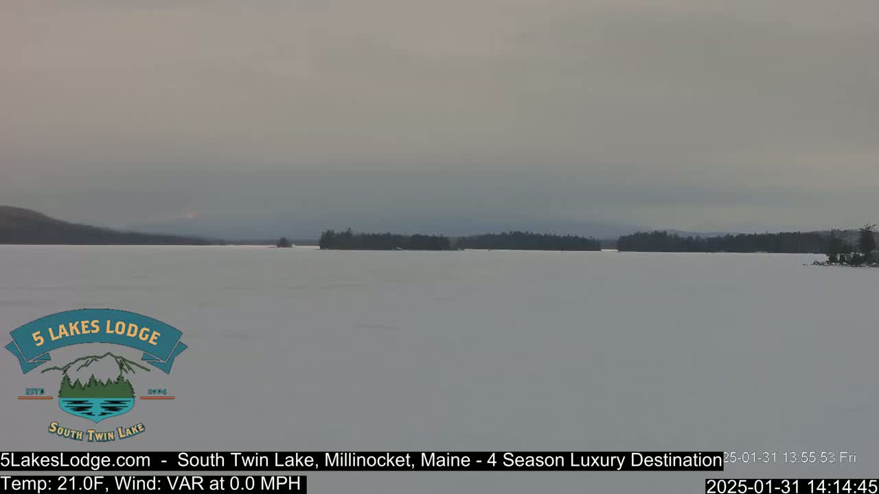 A frozen lake with a distant snow-covered treeline under an overcast sky.