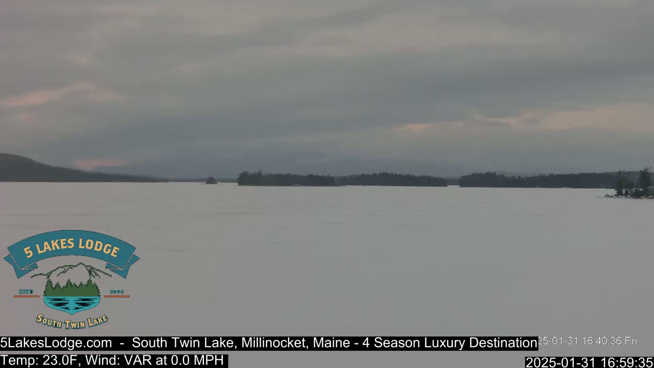 A snow-covered lake stretches to a distant, dark treeline under a cloudy sky.