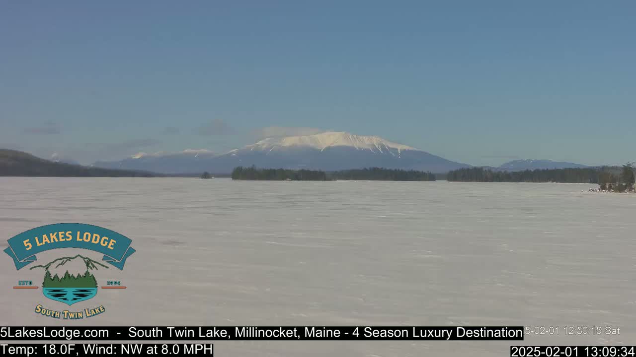 A snow-covered lake stretches to a distant mountain range under a clear blue sky.