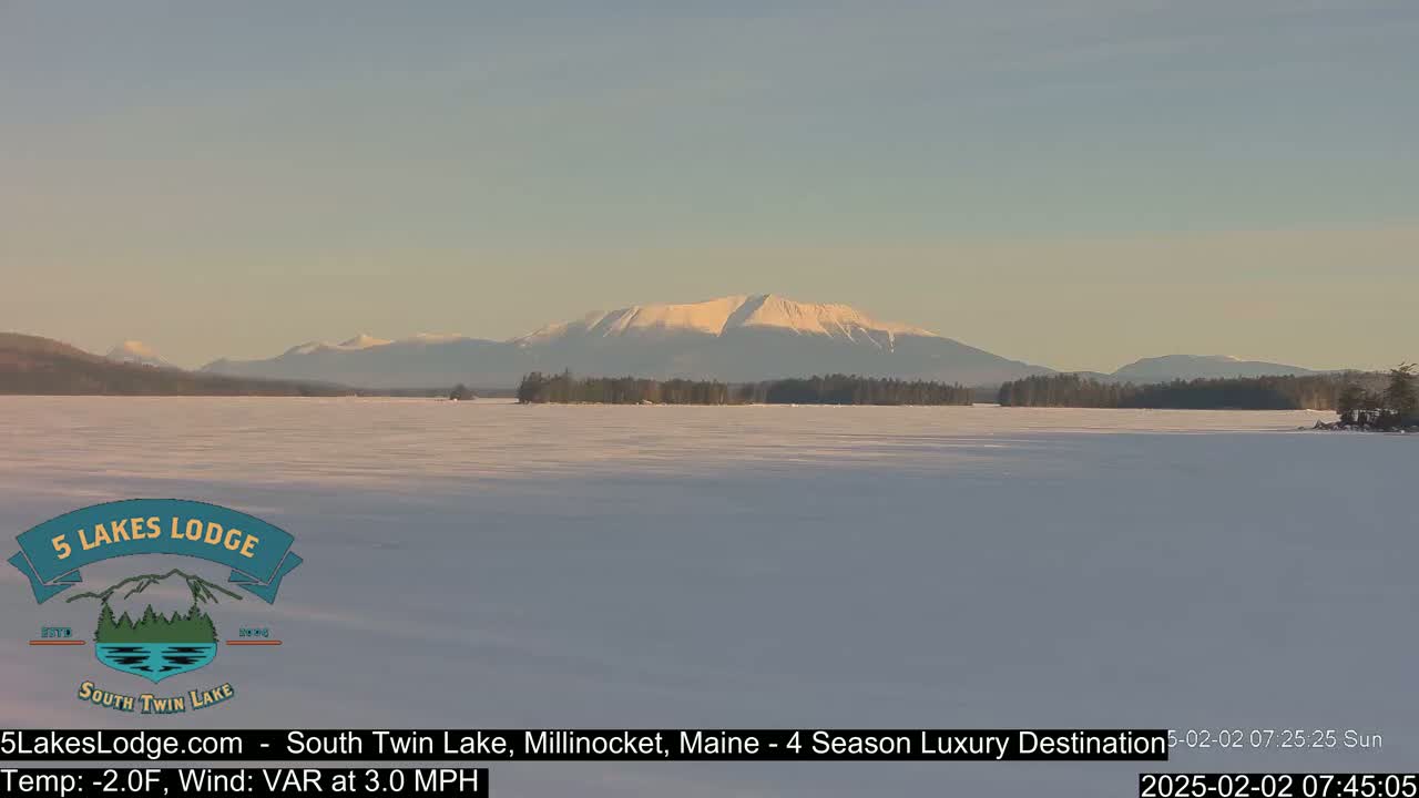 A snow-covered lake stretches to a distant mountain range under a clear, light-blue sky.