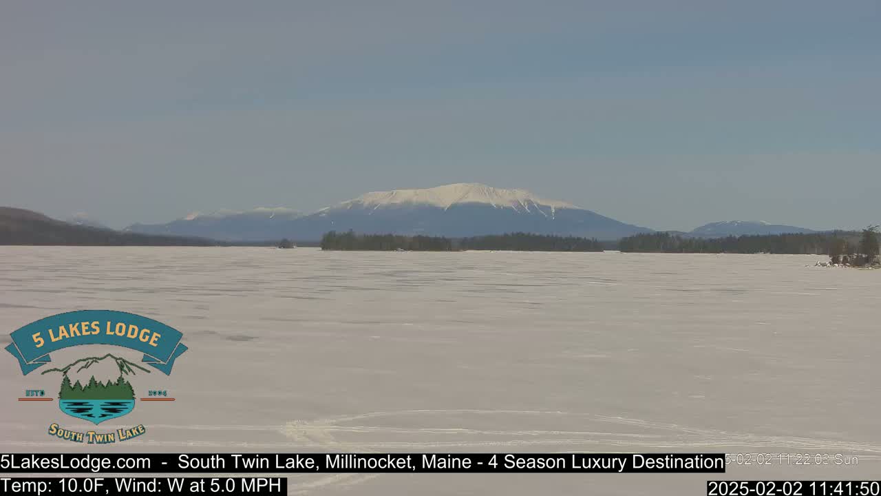 A snow-covered lake stretches to a distant mountain range under a clear, bright sky.