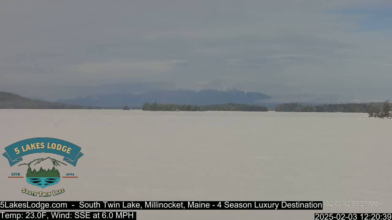 A frozen lake stretches to distant, hazy mountains under a cloudy sky.