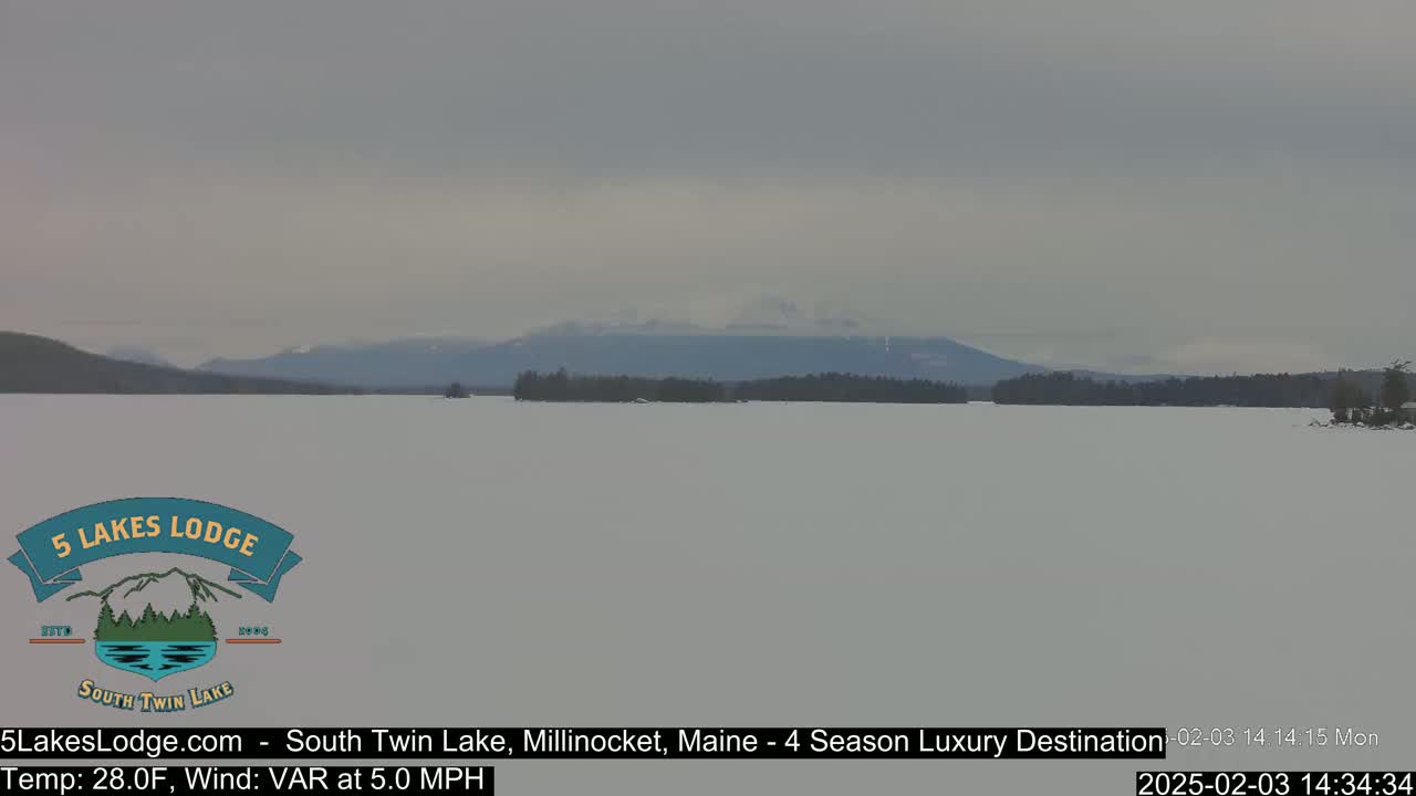 A snow-covered lake stretches to a distant mountain range under a cloudy sky.