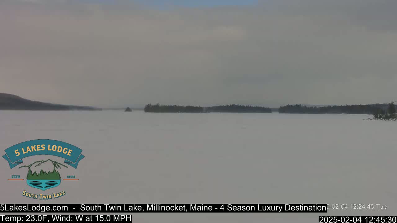 A snow-covered lake with a distant treeline is visible under an overcast sky with a 15 mph westerly wind and a temperature of 23 degrees Fahrenheit.