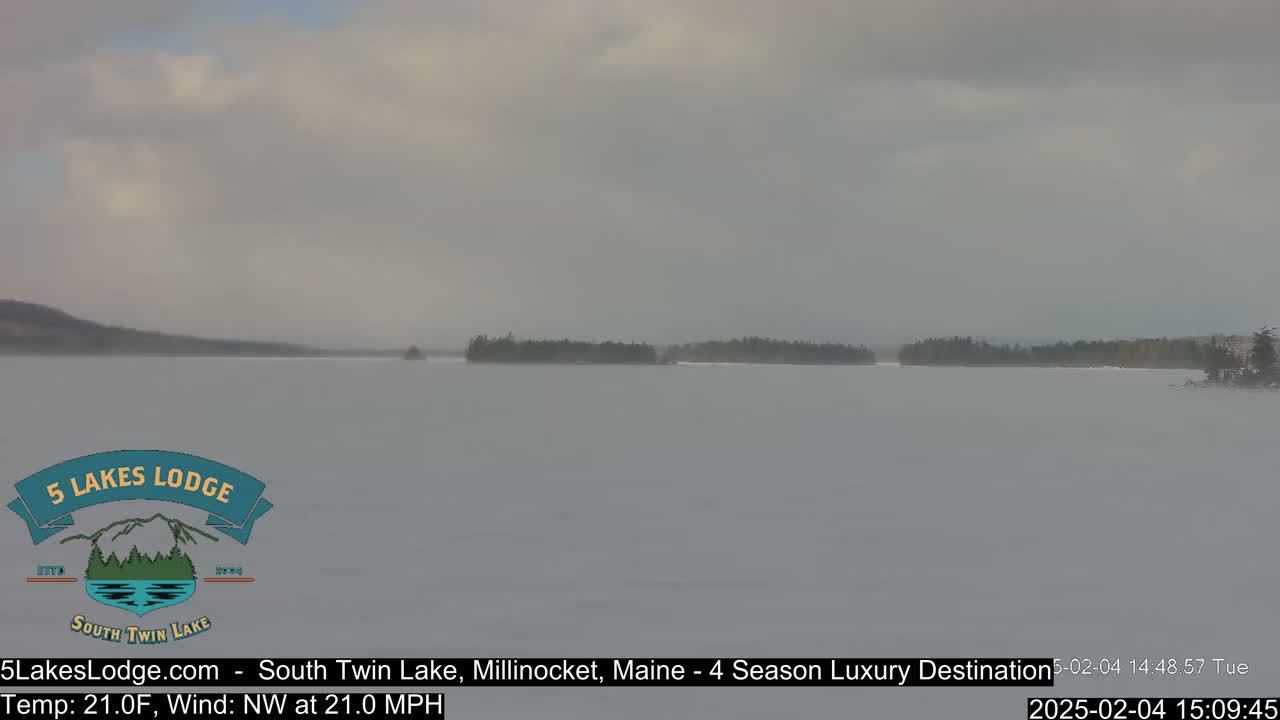A snow-covered lake is visible under an overcast sky, with a distant shoreline of dark trees.