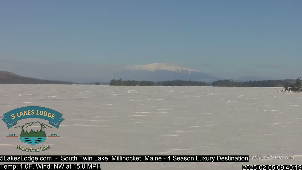 A snow-covered lake stretches to a distant, snow-capped mountain under a clear blue sky.