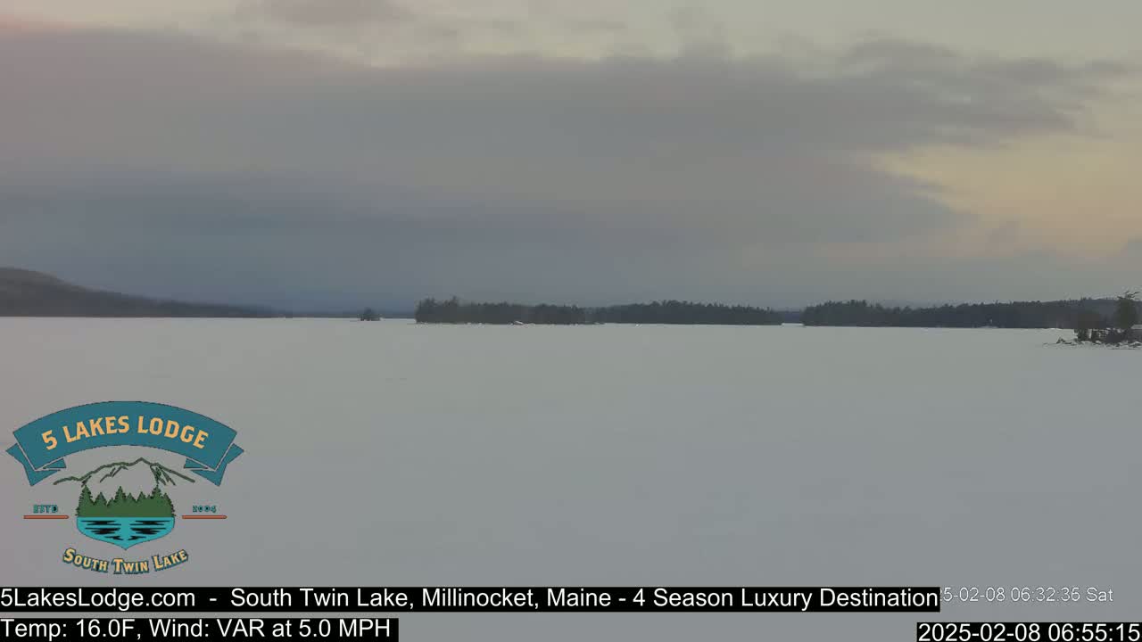 A snow-covered lake stretches to a treeline under a cloudy sky.