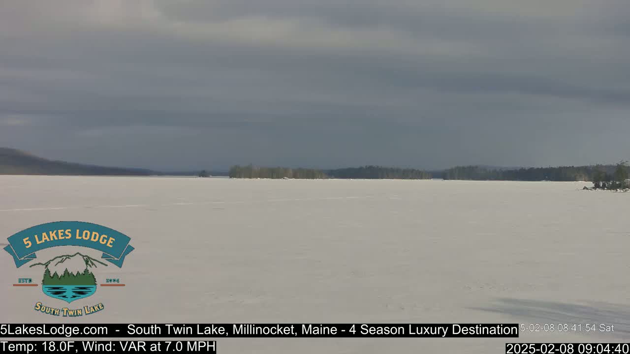 A frozen lake stretches to a distant treeline under a mostly cloudy sky.