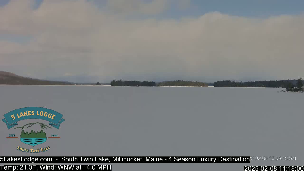 A frozen lake with a distant treeline is visible under a partly cloudy sky.