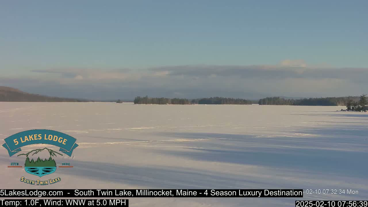 A frozen lake stretches to a treeline under a mostly clear, bright sky.