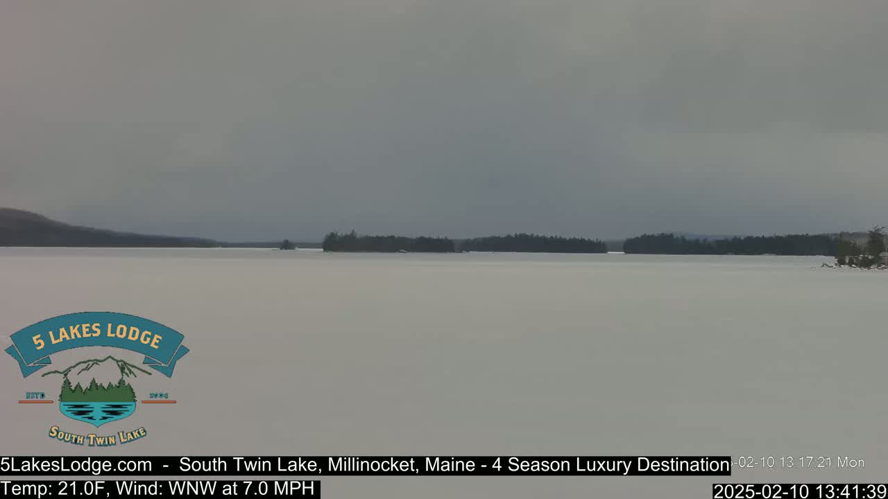 A snow-covered lake stretches to a distant, dark treeline under a gray sky.