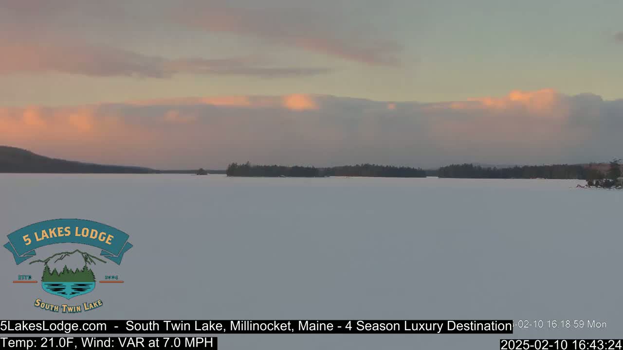 A frozen lake under a pale pink and gray sunset, with a distant tree line.