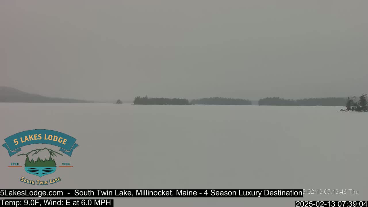 A snow-covered lake is visible, with dark tree lines faintly seen on the far shore under a heavy, gray sky.