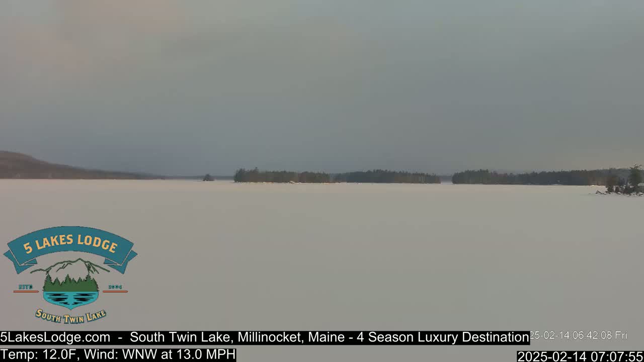 A snow-covered lake stretches to a distant tree line under a hazy sky.