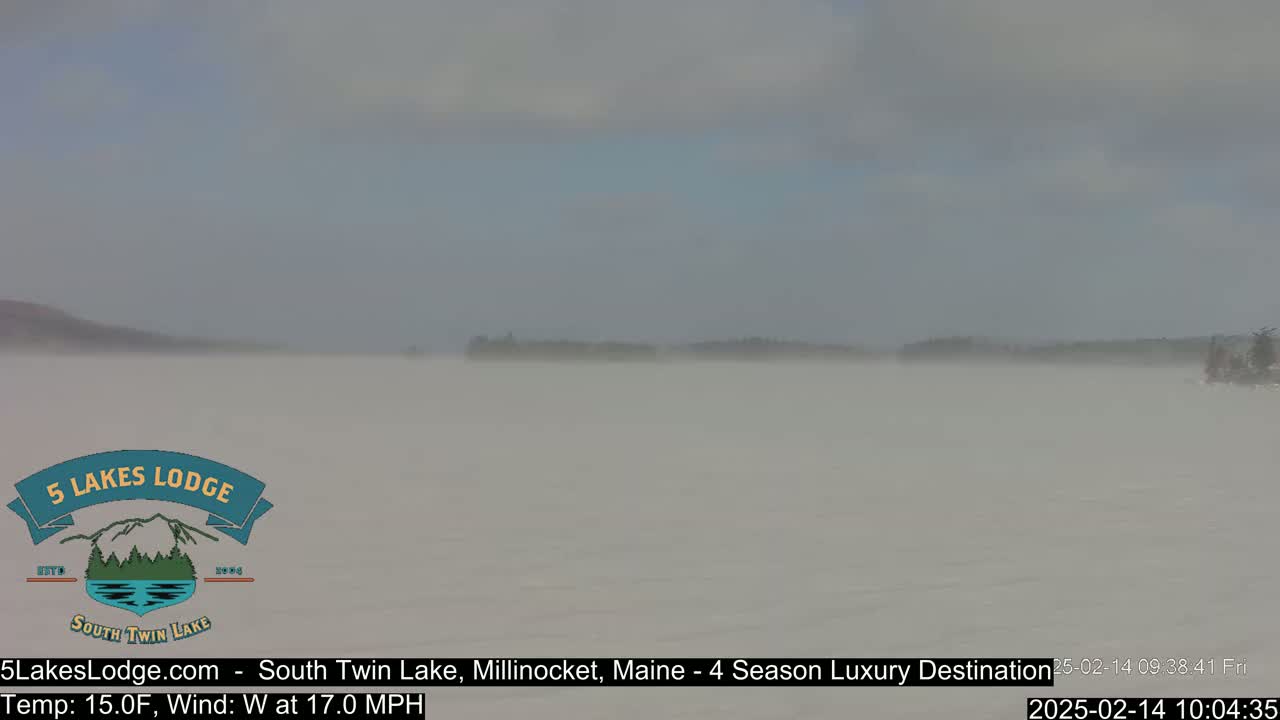 A hazy, foggy lake scene with a distant, indistinct shoreline is visible under a cloudy sky, with a strong westerly wind.
