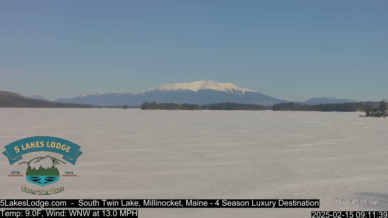 A snow-covered lake stretches to a distant mountain range under a clear blue sky.