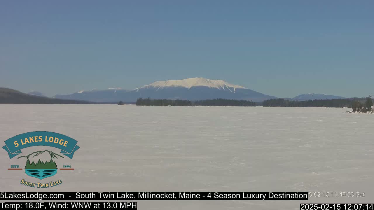 A snow-covered lake stretches to a distant mountain range under a clear blue sky.