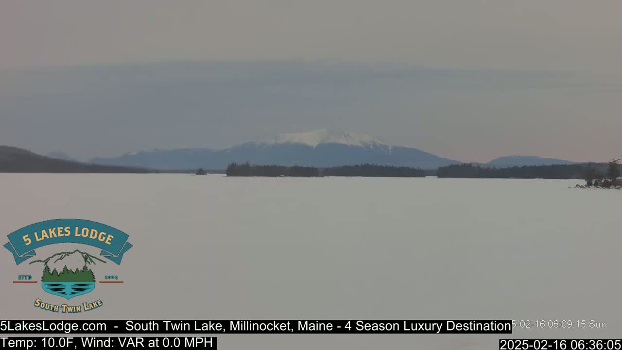 A snow-covered lake stretches to a distant mountain range under a cloudy sky.