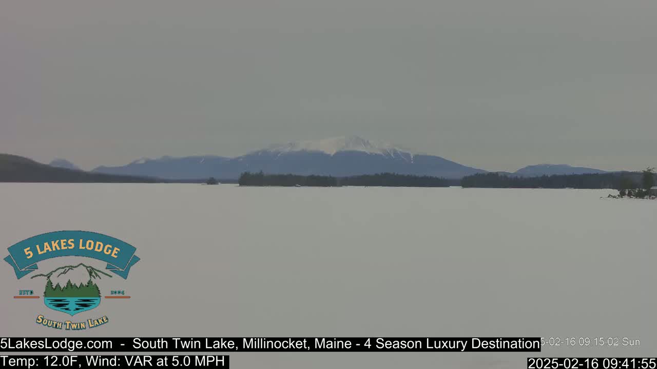 A snow-covered lake stretches to a distant mountain range under a hazy sky.