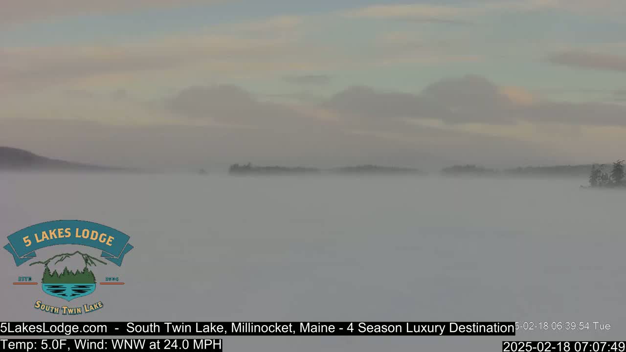 A foggy lake is surrounded by a low, dark treeline under a pale sky.
