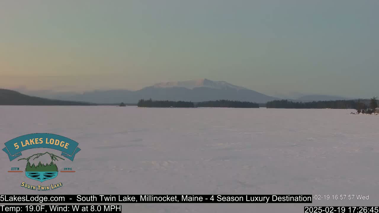 A frozen lake stretches out to a distant mountain range under a pale, twilight sky.
