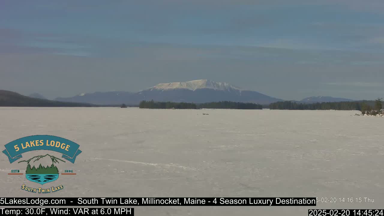 A snow-covered lake stretches to a distant mountain range under a clear, bright sky.