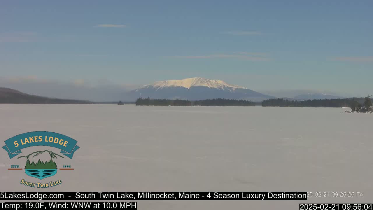 A snow-covered lake stretches to a distant, snow-capped mountain under a clear blue sky.