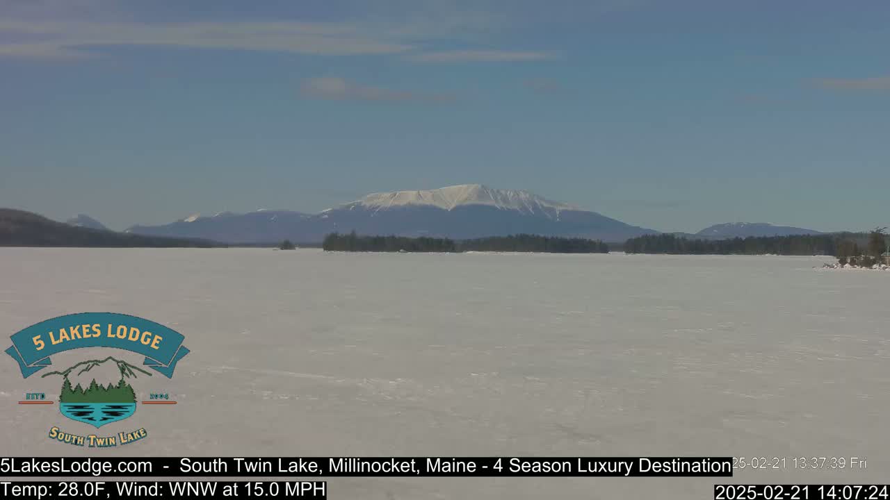 A snow-covered lake stretches to a distant mountain range under a clear blue sky.