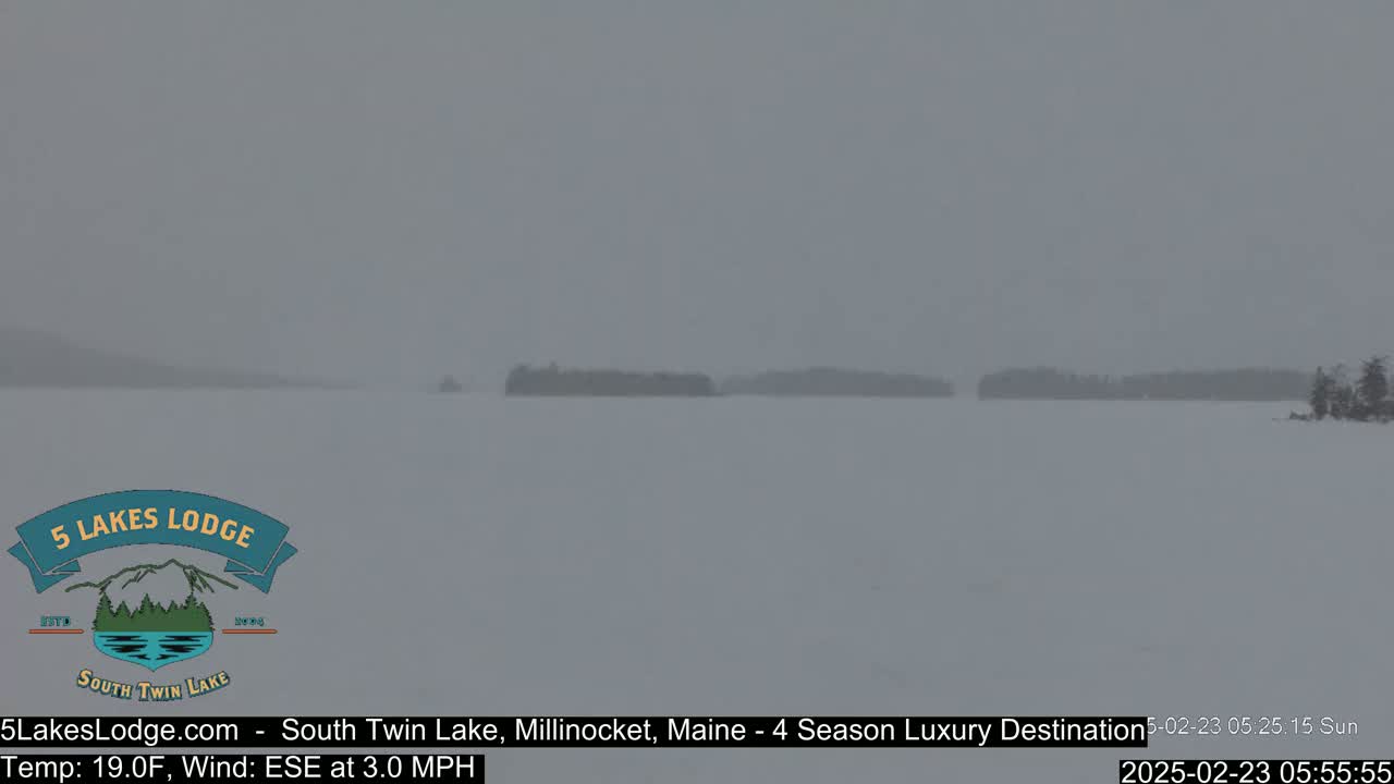 A snow-covered lake with distant islands is visible under overcast skies.