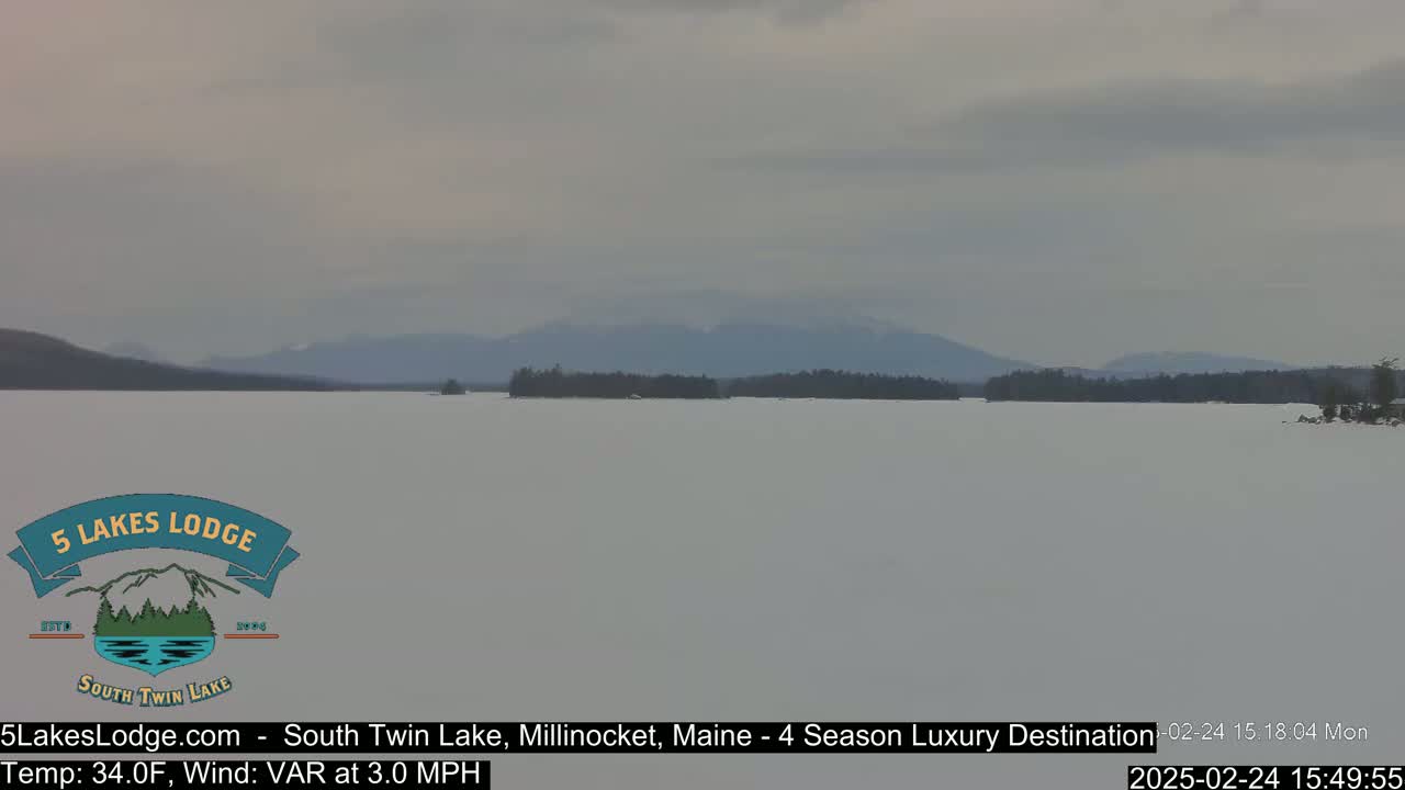 A frozen lake stretches to a distant mountain range under an overcast sky.