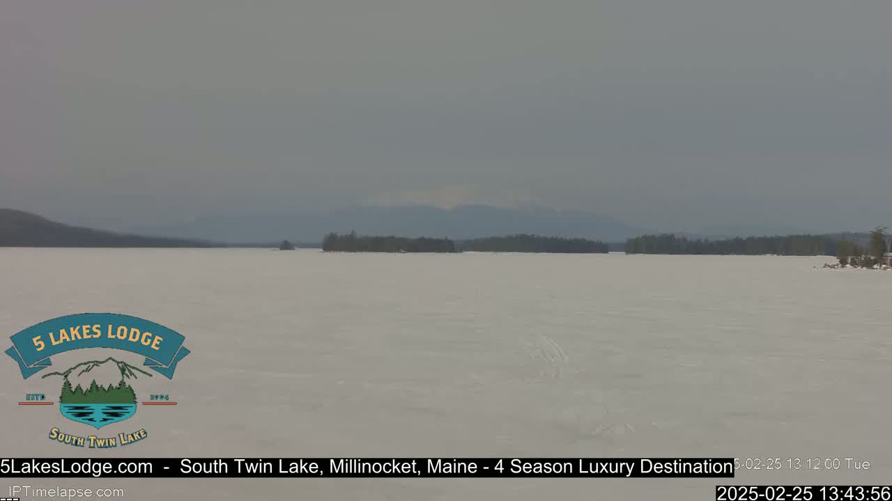 A frozen lake stretches to a distant, hazy mountain range under a gray sky.