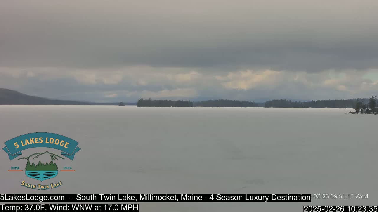 A frozen lake stretches to a distant, tree-lined shore under an overcast sky.