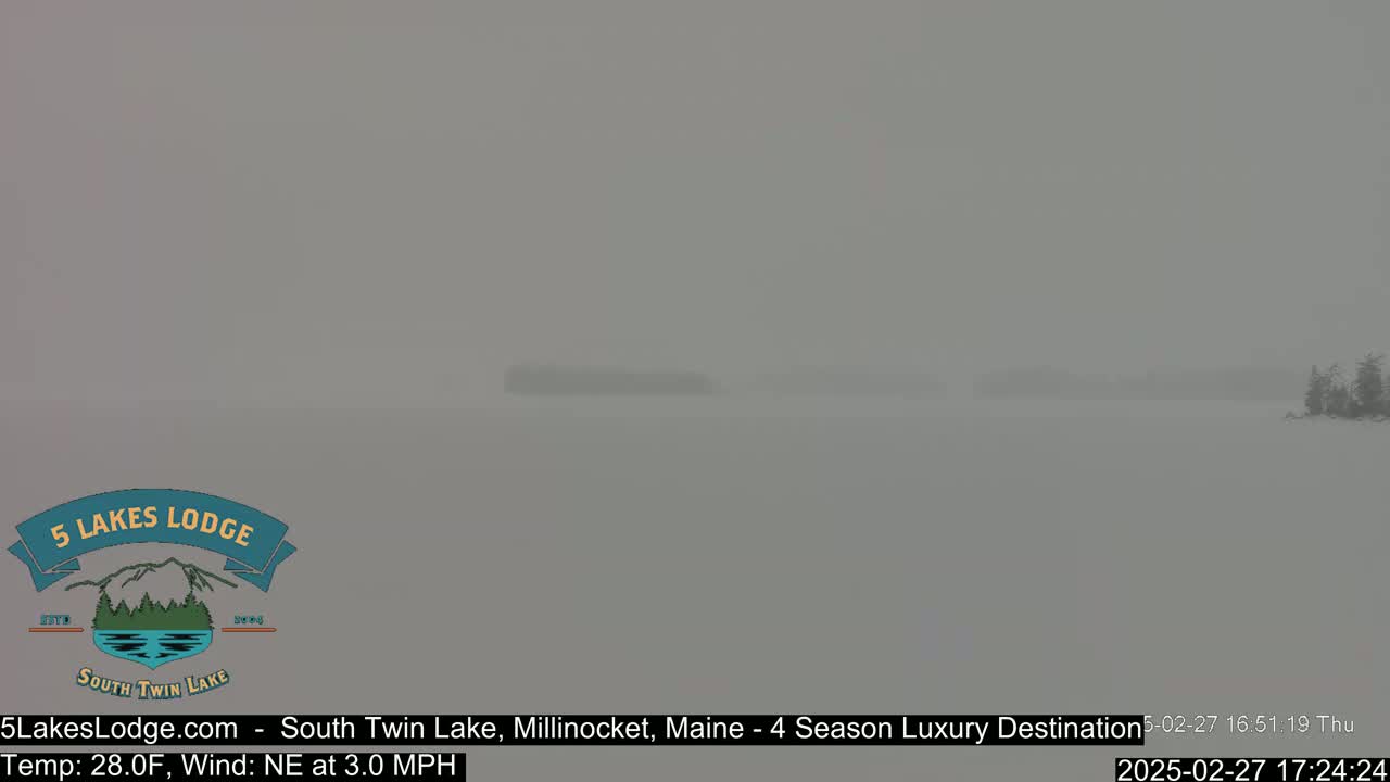 A snow-covered lake is visible in hazy conditions, with a small treeline in the distance.