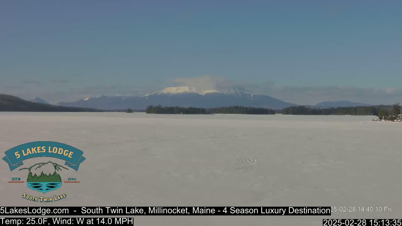 A snow-covered lake stretches out to a distant, snow-capped mountain range under a clear, bright sky.