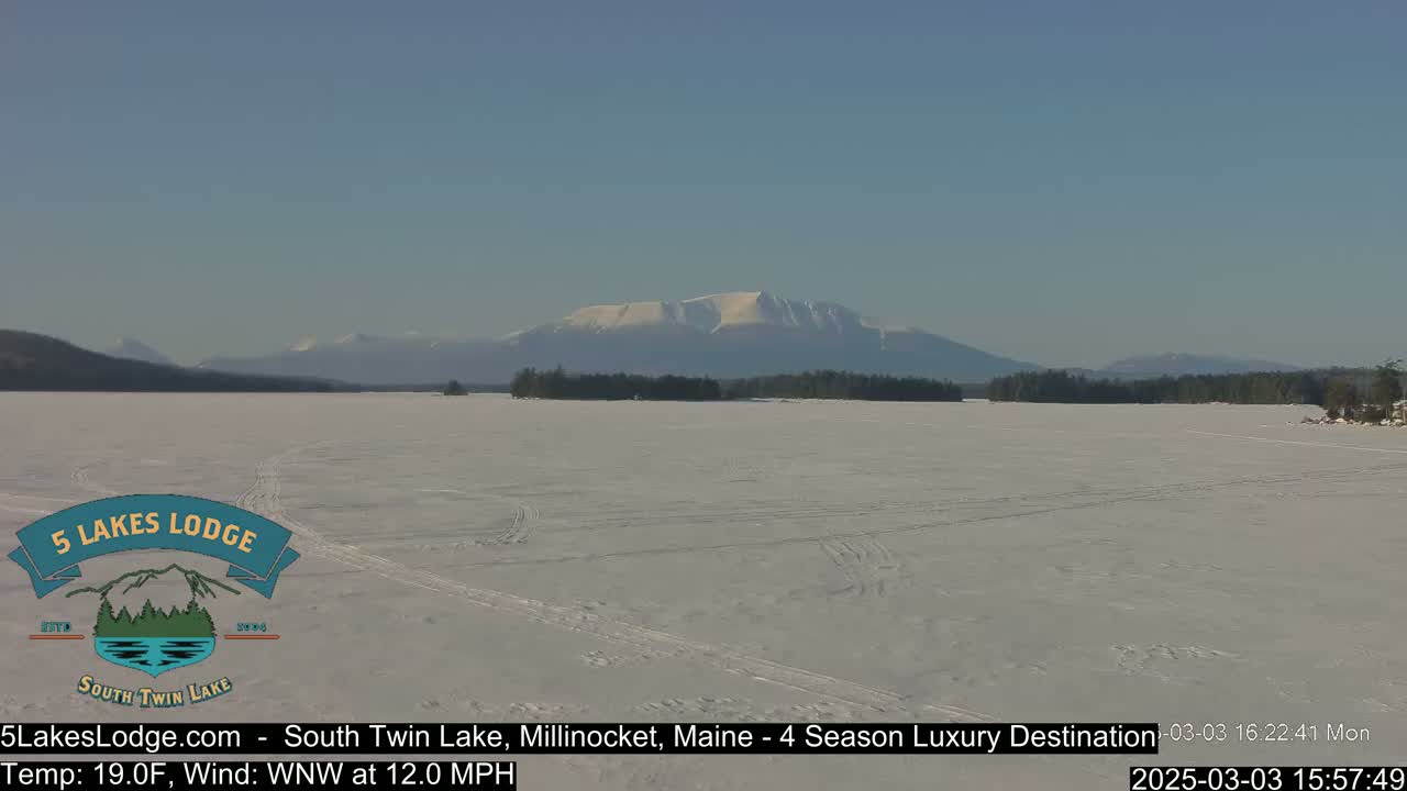 A snow-covered frozen lake stretches to a distant mountain range under a clear blue sky.
