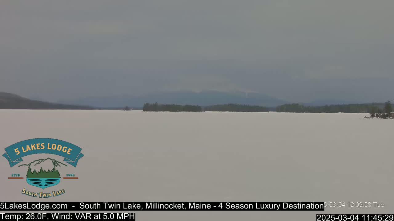 A frozen lake stretches to distant, hazy mountains under an overcast sky.