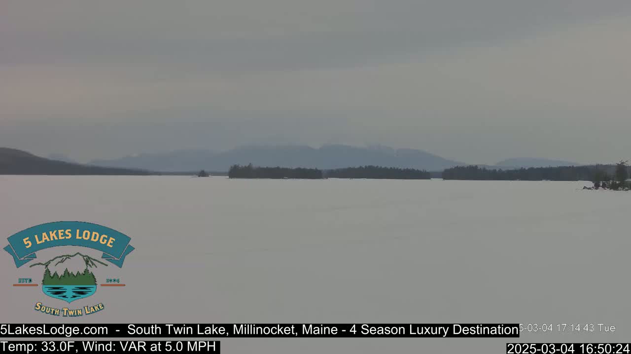 A frozen lake stretches to distant, hazy mountains under a cloudy sky.