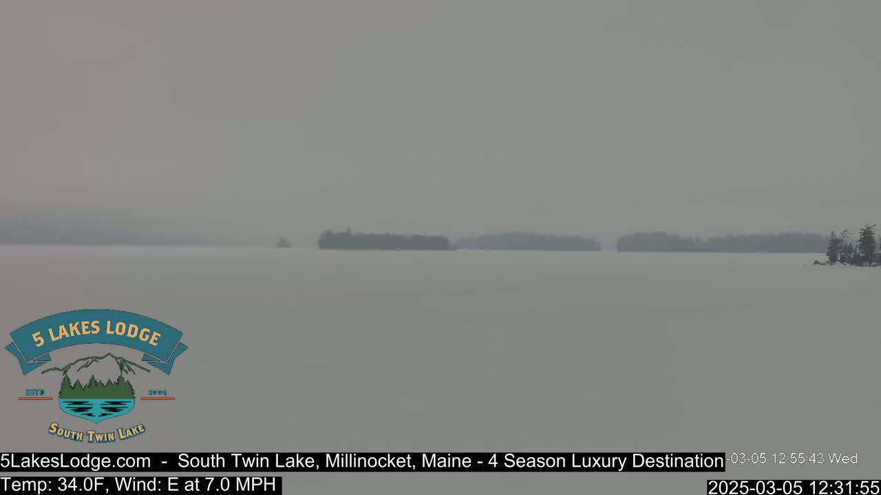 A hazy, snowy view of a lake with distant tree-lined shorelines.