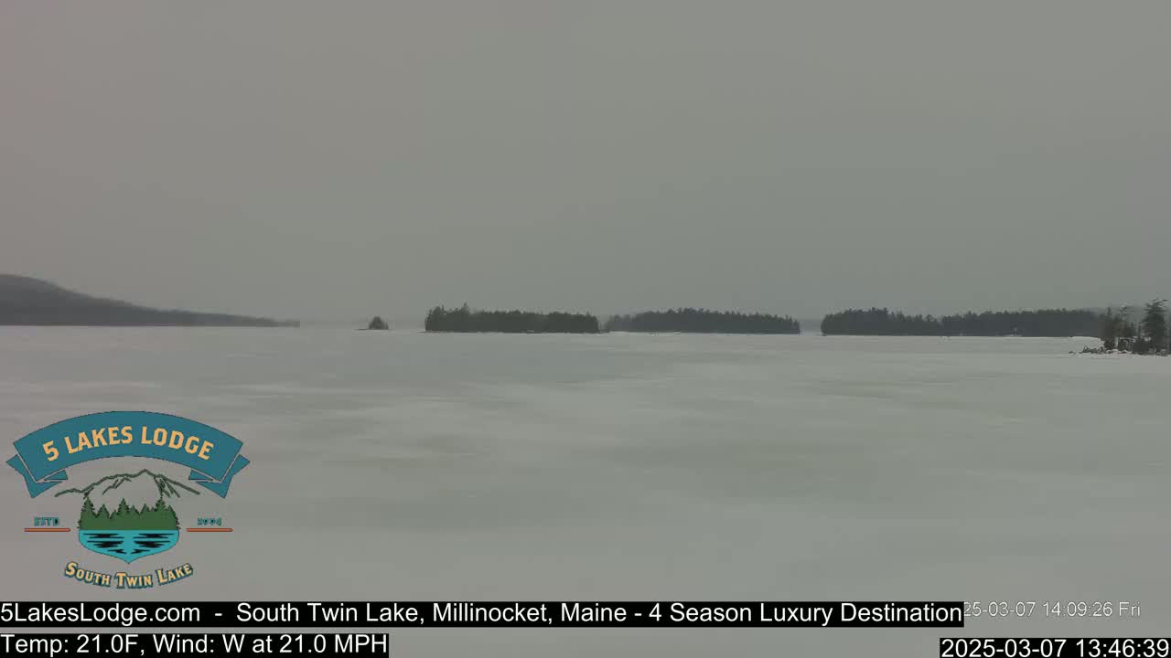 A snow-covered lake with distant tree-covered islands is visible under an overcast sky.